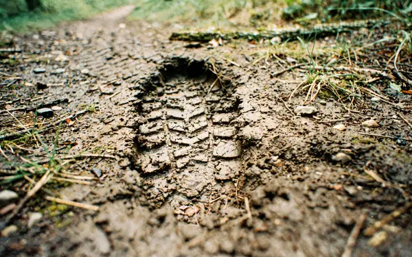 Close-up of a boot print pressed into a muddy trail with grass and detailed treads — 4K Ultra HD PC desktop wallpaper and background.