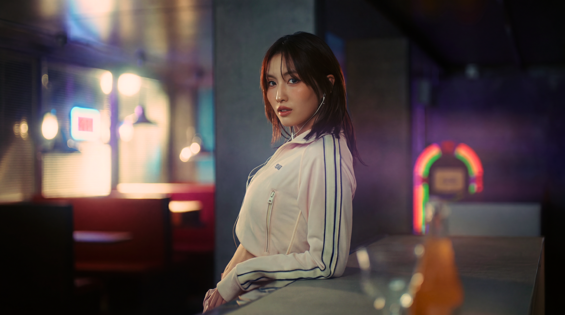 5K Ultra HD desktop wallpaper: moody neon portrait of a Japanese K-pop model in a light track jacket, TWICE/MiSaMo–inspired styling, seated at a dimly lit bar.