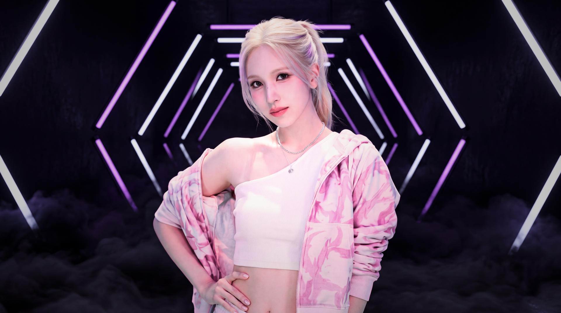 5K Ultra HD PC wallpaper of a blonde model in a pink patterned jacket and white crop top posing confidently against neon geometric stage lights, K-pop–styled.