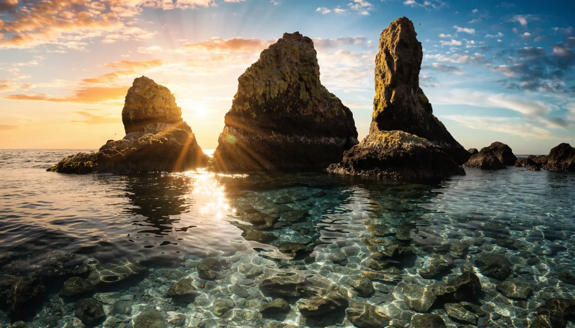 2K Quad HD PC wallpaper: summer ocean with clear shallows and three sea stacks, rocks silhouetted as warm sunset and sunrise hues spilling across the low horizon.