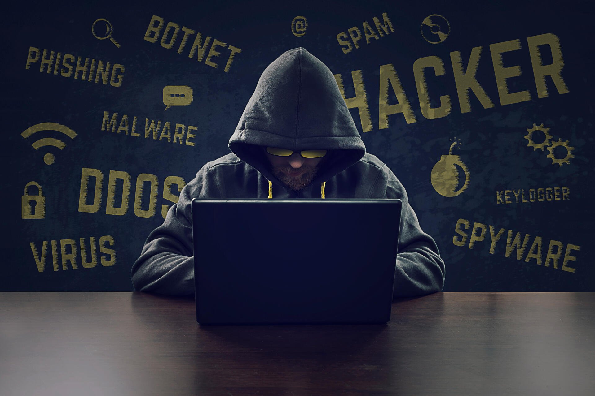 5K Ultra HD PC desktop wallpaper showing a hooded hacker at a laptop in a dark terminal-style background with words: HACKER, DDOS, MALWARE, SPYWARE.