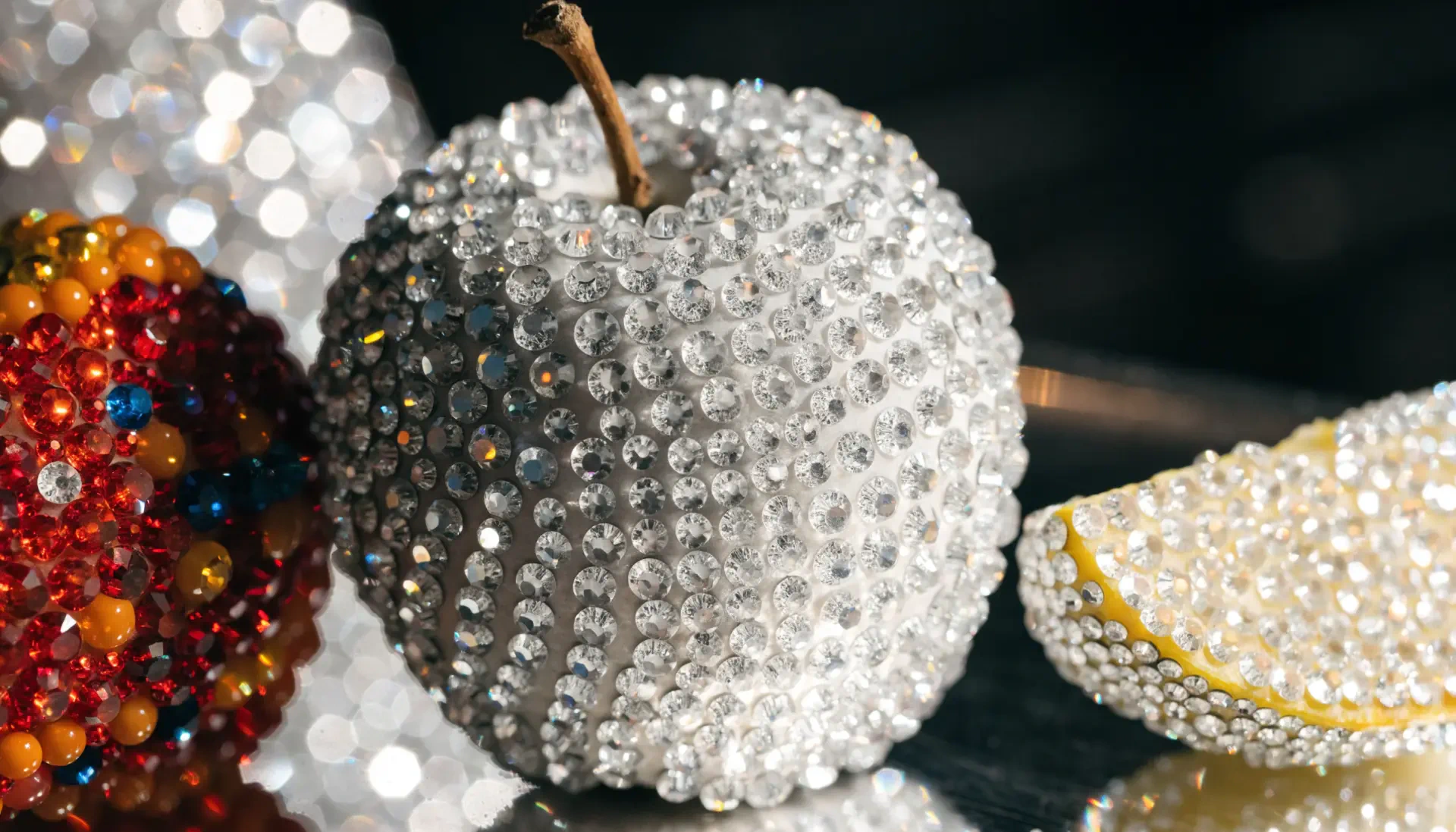 Bedazzled apple encrusted with clear rhinestones beside jeweled fruit, glossy close-up — 2K Quad HD PC desktop wallpaper and background.