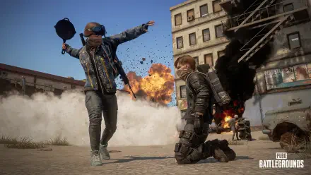 HD PC desktop wallpaper of PlayerUnknown's Battlegrounds: a helmeted player leaps as a kneeling teammate faces explosions, smoke and ruined urban buildings.