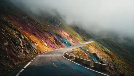 4K Ultra HD desktop wallpaper — winding road through a foggy mountain pass, colorful rocky slopes and low clouds obscuring the peaks.