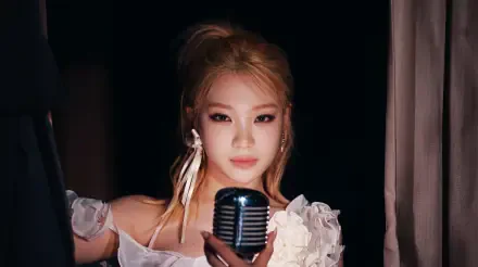 Blonde K-pop idol in a white floral stage outfit holding a vintage microphone against a dark backdrop — 5K Ultra HD PC desktop wallpaper