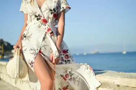 4K Ultra HD PC wallpaper: woman in a laced-up floral dress and straw bag on a sunny beach promenade, dress slit blowing in the sea breeze with sailboats on the horizon.