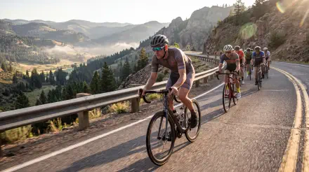 Cyclists riding road bikes along a scenic mountain road, featured in a 5K Ultra HD PC desktop wallpaper and background.