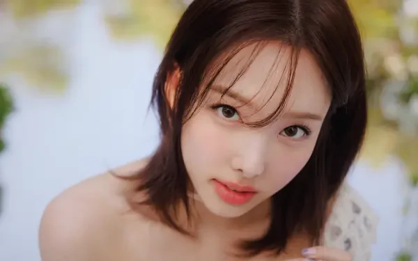Close-up 5K desktop wallpaper of a young woman with shoulder-length dark hair, soft makeup and a gentle expression, looking at the camera against a blurred floral bokeh background.