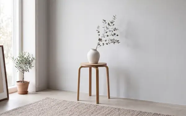 Clean minimalist interior: wooden stool with white vase and sprig, potted plant by a bright window — 5K Ultra HD PC desktop wallpaper and background.