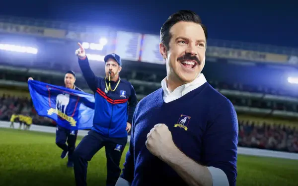 Smiling mustachioed soccer coach pumping his fist as teammates wave a blue flag on a stadium pitch — 4K Ultra HD PC desktop wallpaper and background.