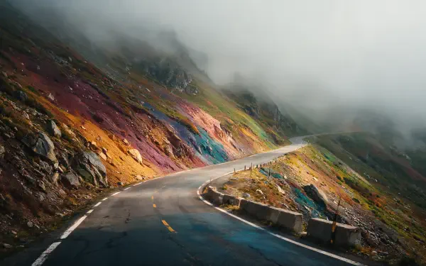 4K Ultra HD desktop wallpaper — winding road through a foggy mountain pass, colorful rocky slopes and low clouds obscuring the peaks.