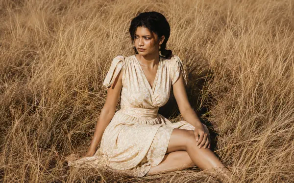 Sunlit portrait of a celebrity actress seated in tall golden grass wearing a cream dress — 4K Ultra HD PC desktop wallpaper/background.