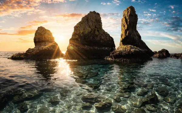 2K Quad HD PC wallpaper: summer ocean with clear shallows and three sea stacks, rocks silhouetted as warm sunset and sunrise hues spilling across the low horizon.