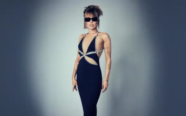 5K Ultra HD desktop wallpaper: singer in a sleek black cutout gown and sunglasses, short tousled hair, posing confidently against a soft gray gradient background.