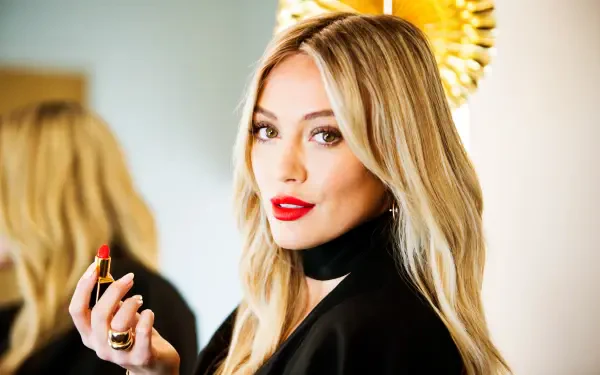 Blonde woman in a black outfit applying red lipstick in a luminous studio portrait — 4K Ultra HD PC desktop wallpaper/background.