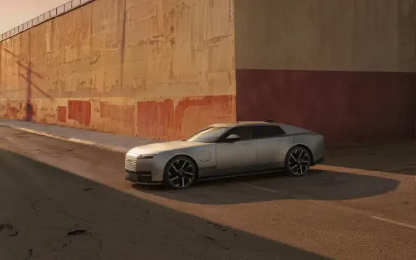Silver Jaguar Type 01 sports car parked beside a sunlit concrete wall, featured in an 8K Ultra HD PC desktop wallpaper and background.