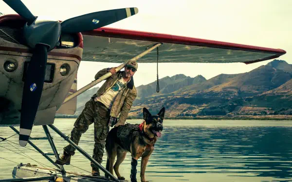 Brad Pitt and a dog beside a vintage airplane on a mountain lake in Heart of the Beast HD desktop wallpaper.