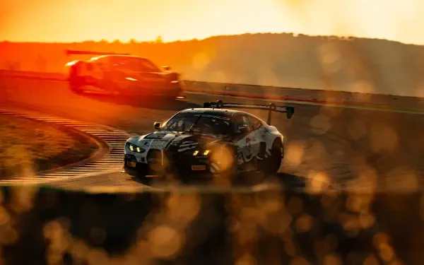BMW M4 GT3 race car drifting through a sunlit track, with dust and motion blur in a dramatic HD desktop wallpaper.