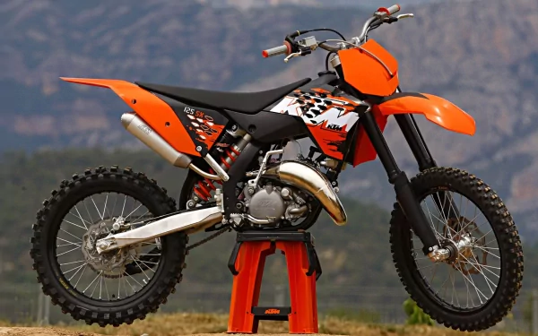 HD PC desktop wallpaper of an orange KTM vehicle — off-road dirt bike on a stand with a mountain backdrop.