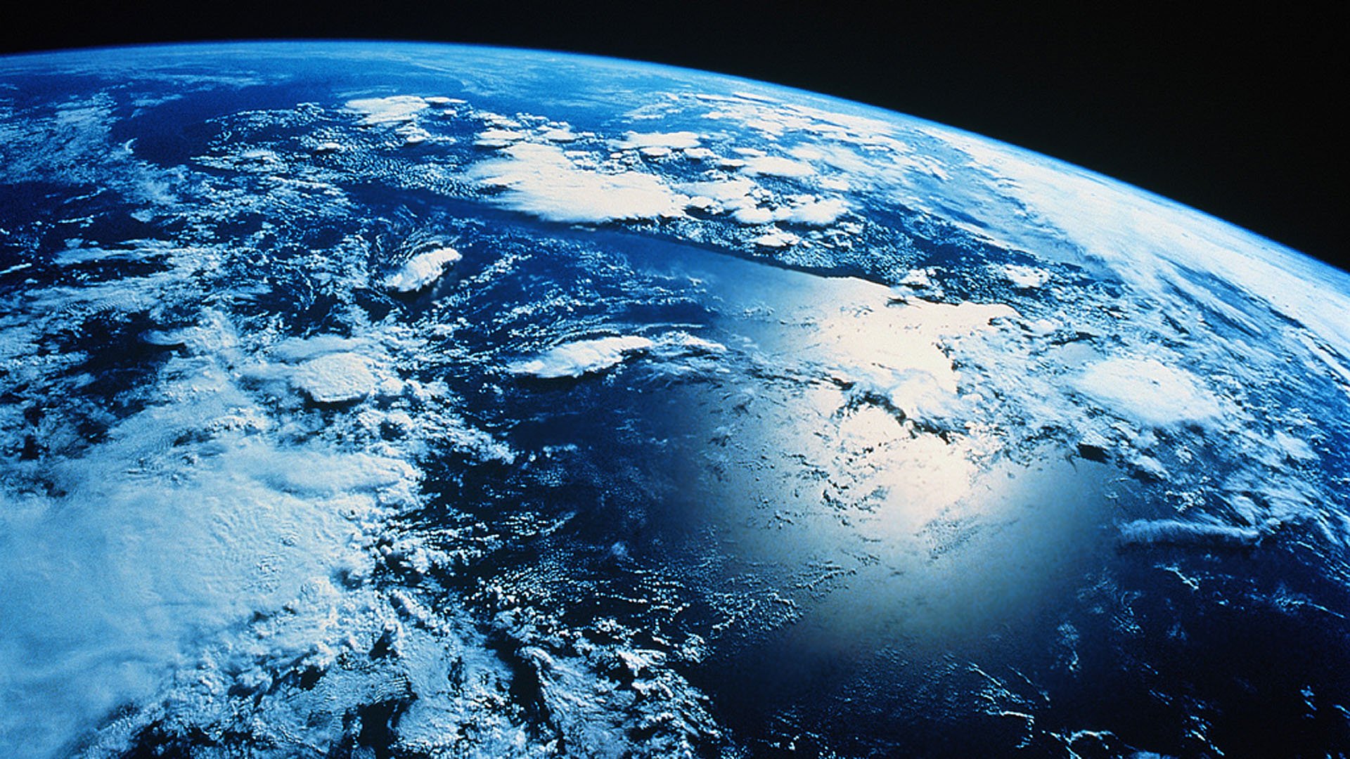 HD PC desktop wallpaper showing Earth’s curved horizon with cloud patterns over vast ocean and land, highlighting nature from space.
