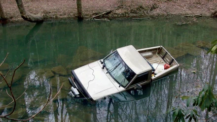 HD desktop wallpaper showing an off-road vehicle partially submerged in a calm, greenish water body surrounded by trees.