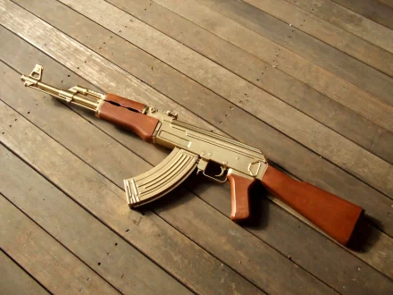 HD desktop wallpaper featuring a man-made AKM assault rifle with wooden accents resting on a wooden floor.