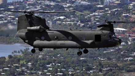 HD desktop wallpaper of a Boeing CH-47 Chinook military helicopter flying over a cityscape, showcasing its twin-rotor design in clear detail.