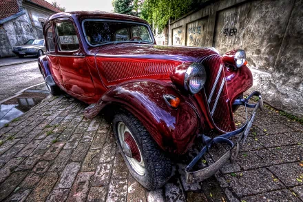 HD desktop wallpaper featuring a classic red Citroën Traction, a vintage French car, parked on a cobblestone street beside an aged wall.