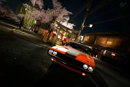 HD PC desktop wallpaper featuring a classic orange muscle car parked on a nighttime street with illuminated buildings and blooming cherry blossom trees.