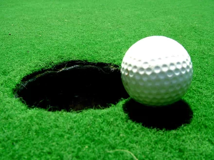 HD PC desktop wallpaper: close-up of a golf ball beside a hole on a bright green putting surface — sports-themed background.