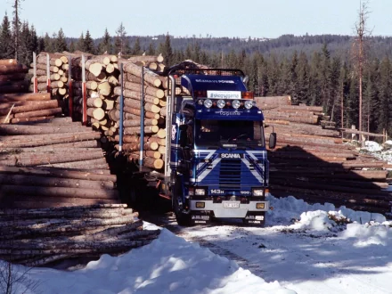 HD desktop wallpaper featuring a Scania vehicle transporting large logs through a snowy forested area.