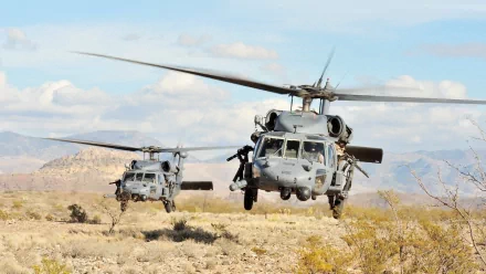 HD desktop wallpaper featuring two military Sikorsky UH-60 Black Hawk helicopters flying low over a desert landscape under a partly cloudy sky.