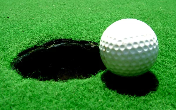 HD PC desktop wallpaper: close-up of a golf ball beside a hole on a bright green putting surface — sports-themed background.