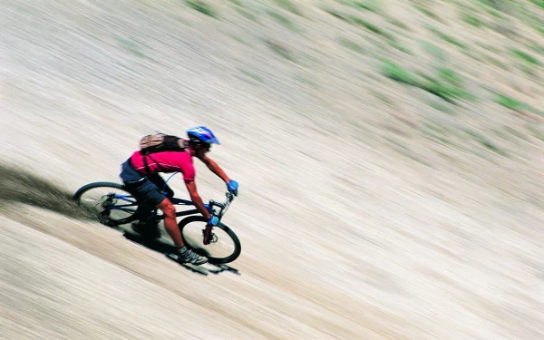 A mountain biker races down a steep, dusty slope, showcasing the thrill of sports and adventure, captured in a dynamic HD desktop wallpaper.