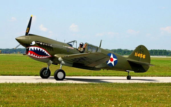 HD desktop wallpaper showing a vintage military aircraft with shark mouth nose art, parked on a runway with clear skies in the background.