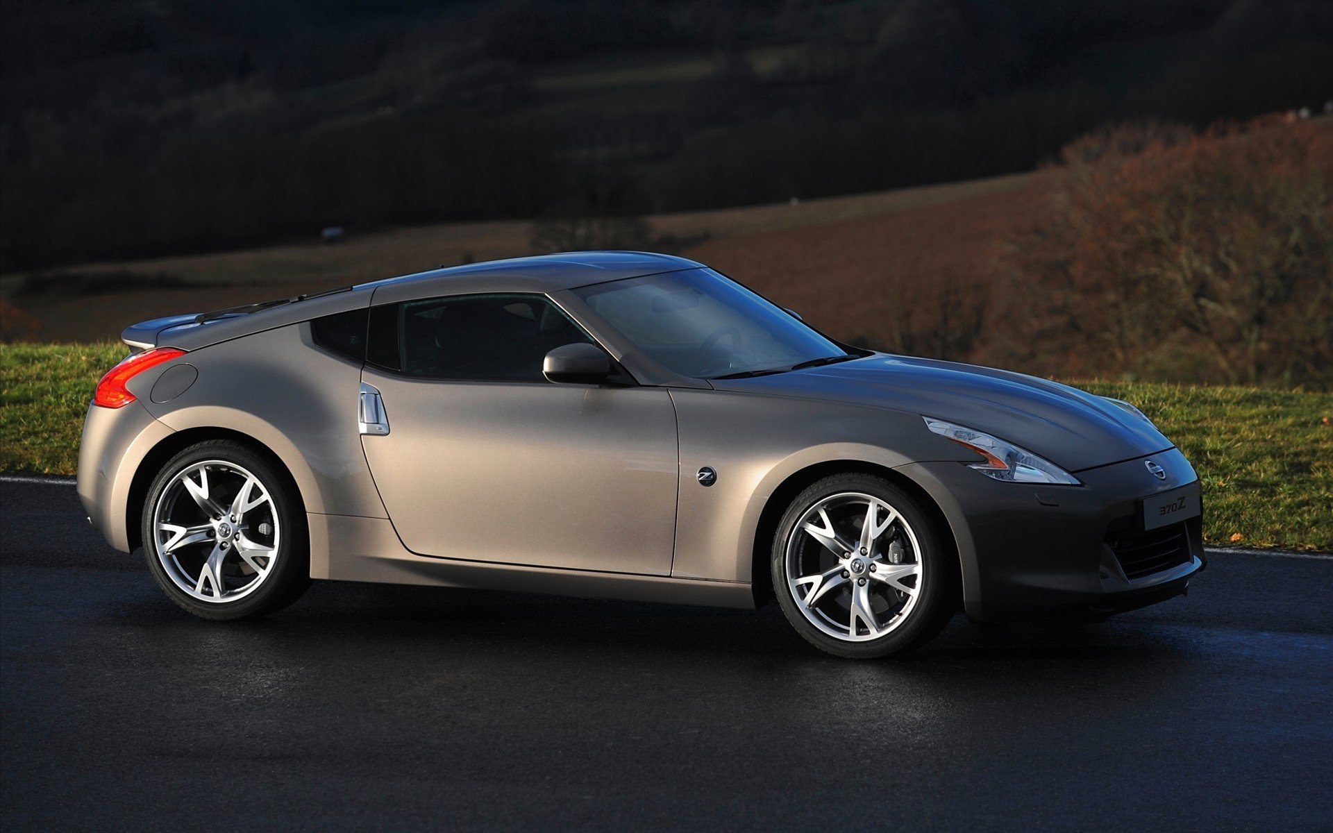 Silver Nissan sports coupe parked on a wet road against rolling hills at dusk — HD PC desktop wallpaper/background.