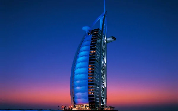 HD desktop wallpaper of Dubai's Burj Al Arab lit in blue at sunset, sail-shaped man-made luxury hotel rising from the sea against a vivid gradient sky.