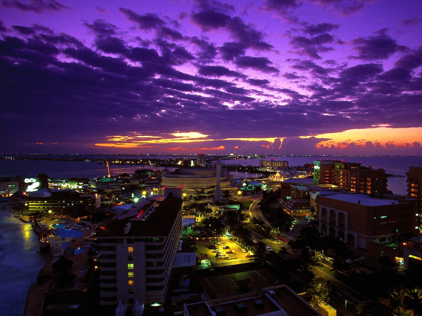 HD PC desktop wallpaper showcasing a vibrant cityscape at twilight with dramatic purple clouds illuminating the man-made skyline.