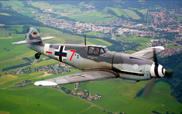 HD desktop wallpaper featuring a military Messerschmitt Bf 109 aircraft flying over a green landscape with a town in the background.