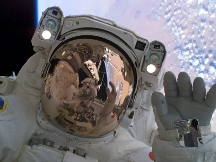 An astronaut in a space suit waves from the void, reflecting Earth and a space station in their visor, showcasing human achievement in space exploration. 