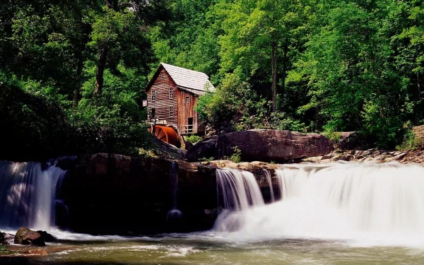 HD PC desktop wallpaper featuring a man-made watermill beside a flowing waterfall, surrounded by lush green trees and natural rock formations.