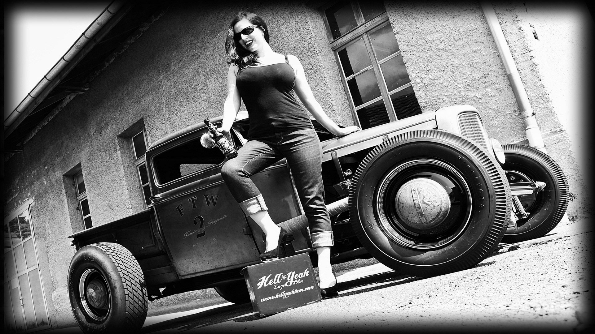 Black and white 4K Ultra HD wallpaper featuring a vintage hot rod car with a woman posing confidently beside it, set against a rustic building backdrop.
