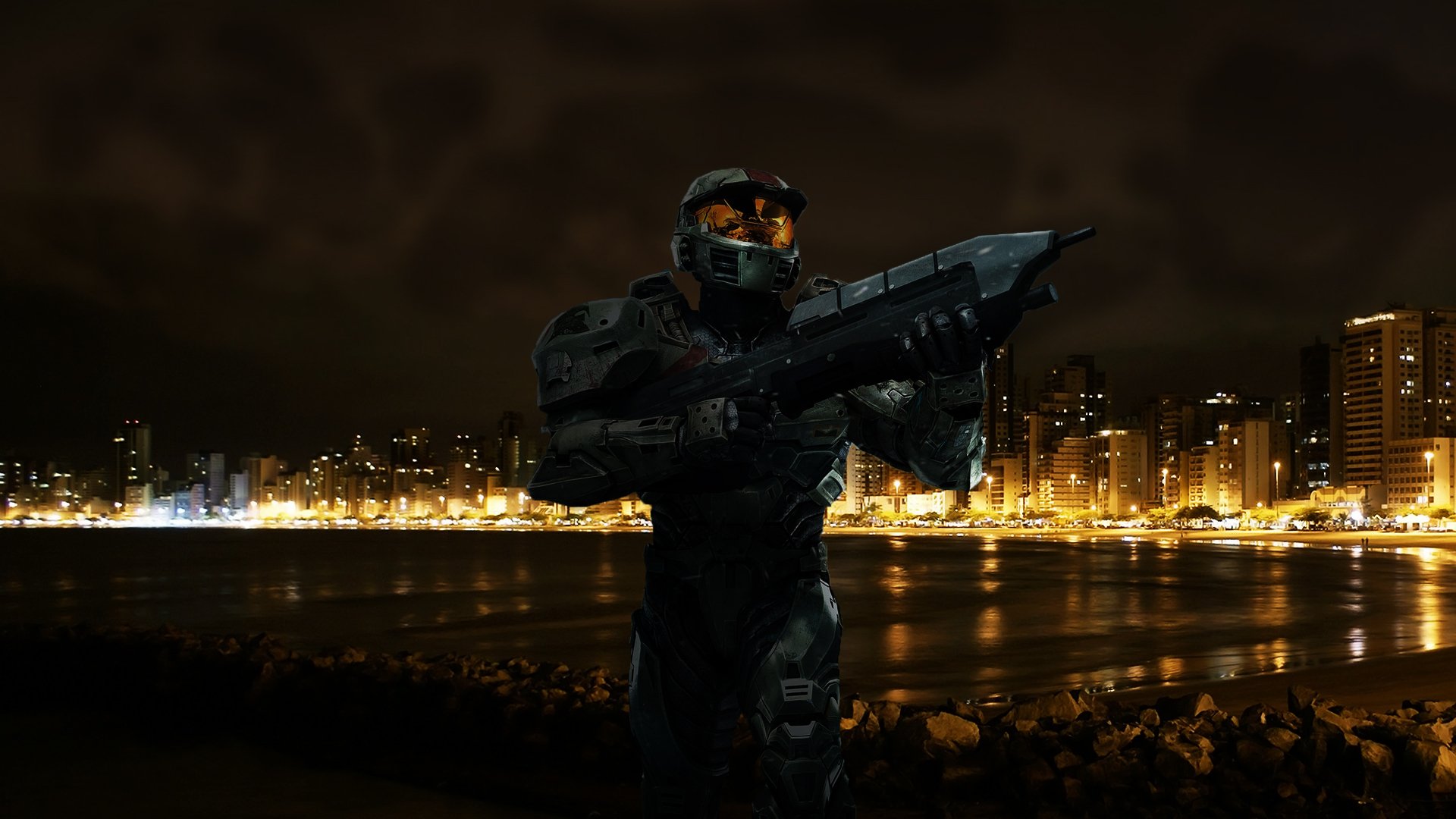 HD PC desktop wallpaper featuring Master Chief from the Halo video game standing in a dark cityscape illuminated by glowing building lights.