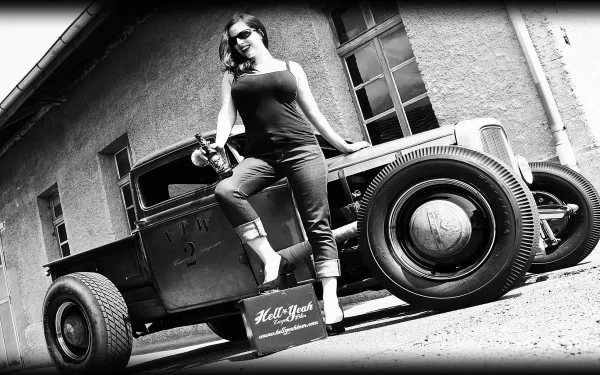Black and white 4K Ultra HD wallpaper featuring a vintage hot rod car with a woman posing confidently beside it, set against a rustic building backdrop.
