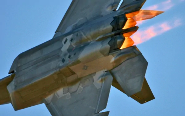 4K Ultra HD PC desktop wallpaper of a Lockheed Martin F-22 Raptor firing afterburners, close rear three-quarter view of the military fighter against a clear blue sky.