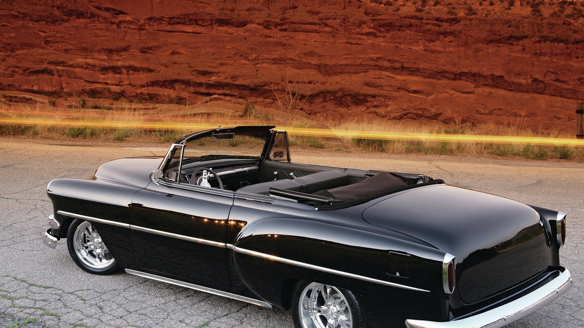 4K Ultra HD PC desktop wallpaper: glossy black classic Chevrolet convertible parked on cracked pavement with red sandstone cliffs in the background.