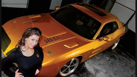 HD PC desktop wallpaper featuring a woman posing beside a shiny orange muscle car in a garage with aGirls & Cars theme.