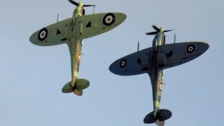 HD PC desktop wallpaper background showing two Supermarine Spitfire military fighters in close formation against a pale blue sky.