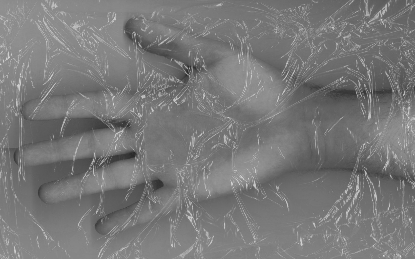 A striking black and white artistic image of a hand partially submerged in water, wrapped in clear plastic, creating a captivating and abstract desktop wallpaper.