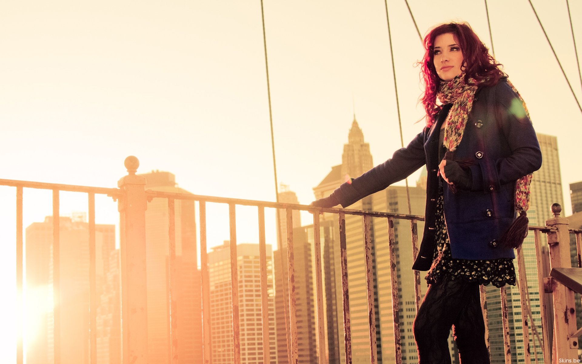 HD desktop wallpaper featuring celebrity Susan Coffey standing on a bridge with a city skyline and warm sunlight in the background.